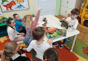 Chłopiec opowiada o ulubionym dinozaurze prezentując jego figurkę.