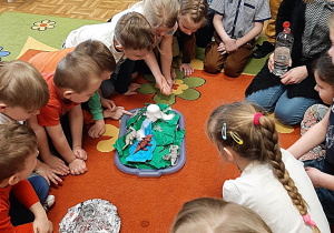 Dzieci siedzą na dywanie, wykonują doświadczenie - wulkan z octu i sody, następne ujęcie.