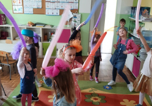 Dzieci tańczą w przedszkolnej sali trzymając lub podbijając kolorowe balony.