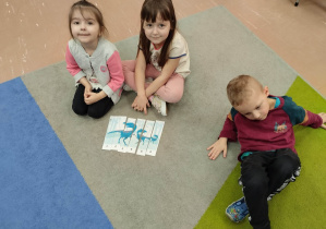 Dzieci siedzą na dywanie i składają obrazek dinozaura z części