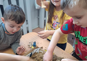 Dzieci przy stoliku szukają szkieletów dinozaurów ukrytych w piasku