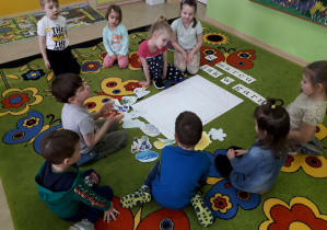 Dzieci na dywanie tworzą plakat "Marcowy garnek".