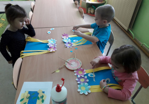 Dzieci przy stolikach naklejają elementy pracy plastycznej "Pani Wiosna".