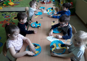 Dzieci przy stolikach wykonują pracę plastyczną "Wilga".