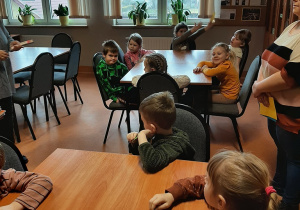 Dzieci podczas spotkania w bibliotece szkolnej, siedzą przy stolikach.
