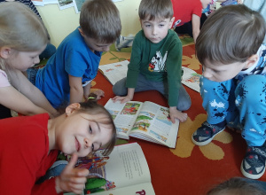 Kilkoro dzieci siedzi na dywanie i ogląda ilustracje do ulubionych bajek w książkach