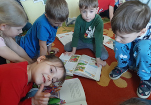 Kilkoro dzieci siedzi na dywanie i ogląda ilustracje do ulubionych bajek w książkach