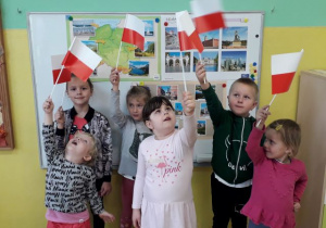 Dzieci trzymają wysoko podniesione flagi polskie.