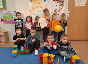 Dzieci podczas wspólnego zdjęcia trzymające zabawki, przyrządy gimnastyczne i rysunki