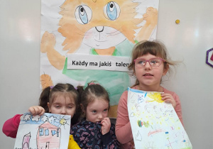 Dziewczynki ze swoimi rysunkami na tle plakatu z kotem Amadeuszem