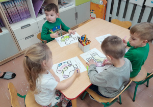 Przedszkolaki przy stolikach kolorują obrazki ze skarpetami