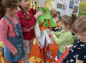 Kilka dziewczynek przystraja w bibułowe paski kukłę Marzannę.