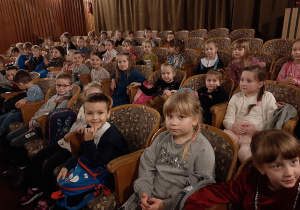 Dzieci siedzą na widowni w sali teatralnej.