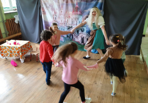 Na scenie - dzieci zaproszone przez aktorkę tańczą z nią w kole. W tle dekoracja.