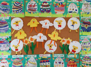 Wystawa przedszkolnych prac plastycznych o tematyce wielkanocnej. Na fotografii widoczne są obrazki z kolorowymi pisankami, baranki, kurczaczki wykonane z papieru.