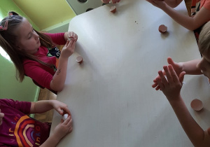 Dzieci przy stoliku wysiewają rzeżuchę do połówek skorupek po jajkach wyłożonych watą.