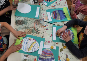 Dzieci z grupy 5,6 latków przy stole malują na kartce wielkanocną pisankę.