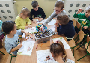 Dzieci z grupy 3,4,5 latków przy stole malują na kartce wielkanocną pisankę.