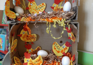 Przedszkolna wystawa w grupie 3,4,5 latków przedstawiająca kartonowy kurnik a w nim kolorowe papierowe kurki i styropianowe jajka.