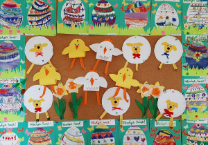 Wystawa przedszkolnych prac plastycznych o tematyce wielkanocnej. Na fotografii widoczne są obrazki z kolorowymi pisankami, baranki, kurczaczki wykonane z papieru.