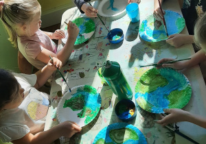 Dzieci z grupy 5,6 latków wykonują sylwetę ziemi malując farbą papierowe talerzyki.
