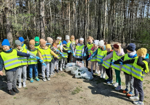 Dzieci z grupy 5,6 latków na leśnej ścieżce prezentują worki z zebranymi odpadami.