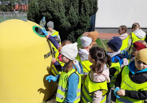 Dzieci wrzucają plastikowe odpady do żółtego pojemnika.