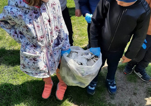 Dzieci z grupy 3,4,5 latków zbierają odpadki na terenie placu przedszkolnego, pakują je do plastikowych worków.