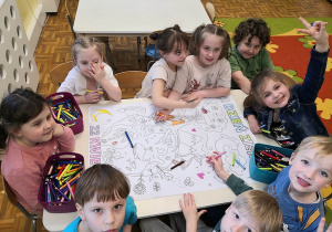 Grupa dzieci przy stoliku koloruje plakat o Dniu Ziemi.