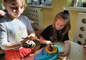 Dwie dziewczynki bawią się gliną. Próbują wykonać naczynie gliniane używając koła garncarskiego - zabawki.