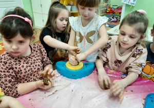 Grupa dzieci podczas zabawy gliną, przy kole garncarskim.