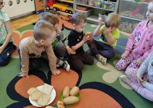 Dzieci siedzą na dywanie i oglądają różne rodzaje pieczywa.