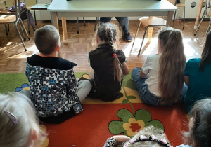 Dzieci siedzą na dywanie, pani bibliotekarka czyta bajkę "Słowik" korzystając z teatrzyku kamishibai - inne ujęcie.