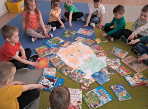 Dzieci z grupy młodszej siedzą w kręgu z plakatem kota Amadeusza i książkami