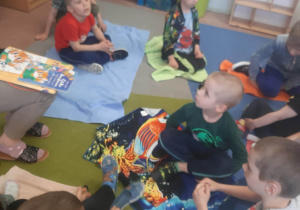 Dzieci siedzą na ręcznikach i słuchają opowiadania