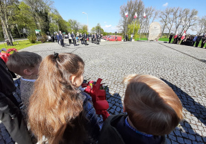 Obchody święta Konstytucji 3 maja. Troje dzieci tyłem do obiektywu, spoglądają na obelisk w Starym Gostkowie.