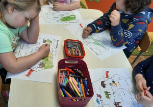 Dzieci w sali przedszkolnej przy stoliku rysują na konturach mapy Polski.