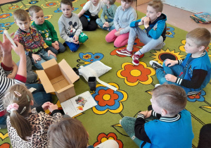 Dzieci siedzą na dywanie i oglądają zawartość pudełka