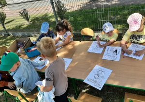 na powietrzu. Dzieci kolorują obrazki siedząc przy stolikach.