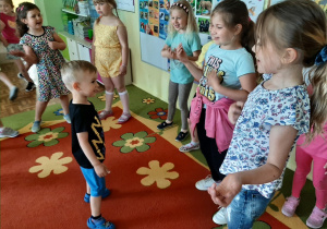 Przedszkolaki wraz z gośćmi podczas zabawy przy muzyce. Dzieci pokazują ruchy ilustrujące treść piosenki.