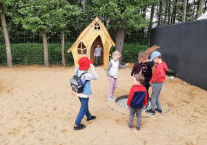 Dzieci na placu zabaw, w tle drewniany domek do zabawy.