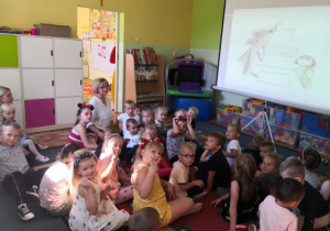 Przedszkolaki siedzące na dywanie przed dużym ekranem i oglądające film edukacyjny.