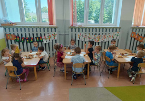 Przedszkolaki siedzą przy stolikach w czasie poczęstunku