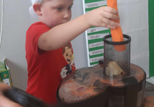 Chłopiec podczas wrzucania marchewki do sokowirówki