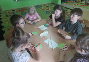 Dzieci przy stolikach składają kasztanek z wyciętych papierowych elementów.