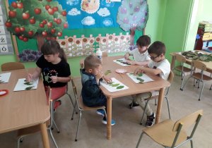 Przedszkolaki przy stolikach z zasuszonych liści tworzą jesienny obrazek.