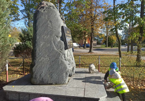 Dwoje dzieci kładzie znicz przy obelisku w Wartkowicach.
