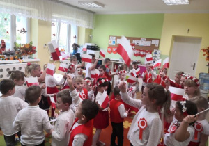 Przedszkolaki maszerują, machają flagami i śpiewają piosenkę.