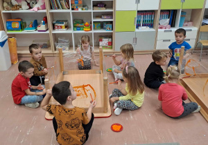 Dzieci w czasie zabawy plastycznej malują pomarańczową farbą na foli