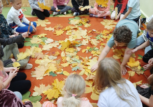 Grupa dzieci siedzi na dywanie w kole. na środku dywanu leżą jesienne liście. Kolejne ujęcie.